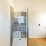Dusche mit Glaswand, Fliesenwand und Waschbecken mit Spiegelschrank.