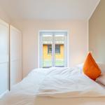 Schlafzimmer mit Bett, Fenster und Wandbild. Links Schrank, rechts Kissen.