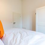 Schlafzimmer mit weißem Bett und orangefarbenem Kissen. Weiße Türen und Wände.