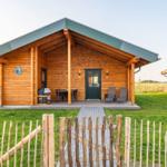 Holzhaus mit Terrasse, Garten und Holzzaun. Tür und Fenster sind dunkel.