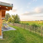 Holzhaus mit Terrasse, Liegestühle und Blick auf grünes Feld.