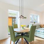 Essbereich mit runden Tisch und grünen Stühlen, Wohnbereich mit Sofa und Fenstern.