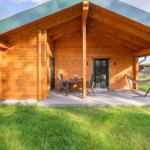 Holzhaus mit Terrasse, Tisch, Stühlen und Hängemöbel. Grasfläche und Zaun im Hintergrund.