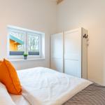 Schlafzimmer mit Bett, Fenster und Kleiderschrank. Draußen ist ein Holzhaus sichtbar.