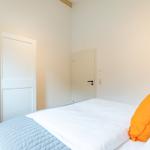 Schlafzimmer mit Bett, orangefarbenem Kissen und weißen Wänden.