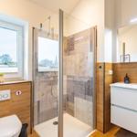 Bad mit Dusche, Waschbecken und Toilette. Fenster mit Blick nach draußen.