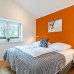 Schlafzimmer mit Bett, Fenster und orangeer Wand. Wandbild zeigt einen Fuchs.