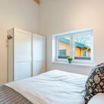 Schlafzimmer mit Bett, Kleiderschrank und Fensterblick auf Holzhaus.