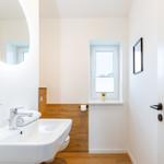 Badezimmer mit Waschbecken, Spiegel, Toilette und Fenster.