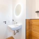 Badezimmer mit Waschbecken, runden Spiegel und Holzwandverkleidung.