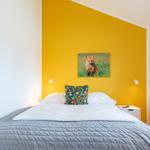 Schlafzimmer mit gelber Wand, Bett und Wandbild eines Fuchses.