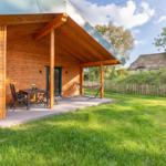 Holzhaus mit Terrasse, Tisch, Stühlen und Hängematte. Grasfläche und Zaun im Hintergrund.