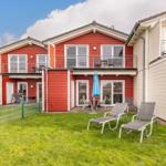 Red vacation home with balcony, garden, and sun loungers. Blue umbrella and terrace.