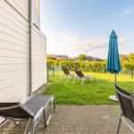 Terrace with lounge chairs and blue umbrella. Lawn and fence in the background.