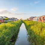 Channel with tall grass and colorful houses on both sides.