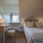 Schlafzimmer mit Doppelbett, Schreibtisch und Fenster. Decke ist schräg.