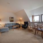 Wohn- und Essbereich mit Sofa, Sessel und Fenstern. Holztisch und Stühle. Spielzeug Schaf.