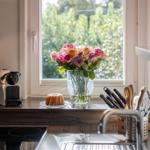 Küchenfenster mit Blumen und Kuchen auf der Arbeitsplatte.