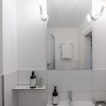 Badezimmer mit Spiegel, Dusche und Waschbecken. Weiße Wände und moderne Beleuchtung.