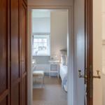 Schlafzimmer mit Bett, Nachttisch und Fenster. Holztüren und Waschmaschine sichtbar.