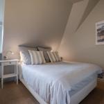 Schlafzimmer mit Bett, Nachttisch und Fenster. Decke geneigt. Wandbild an der Wand.