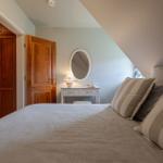 Schlafzimmer mit Bett, Schminktisch und Holztüren unter Dachschrägen.