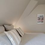 Schlafzimmer mit Bett, Kissen und Wandbild unter schrägem Dach