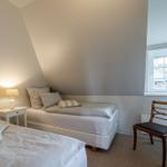 Zimmer mit zwei Betten, Nachttisch, Stuhl und Fenster mit Vorhang.