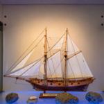 A model of a sailing ship with white sails and wooden structure on a base.