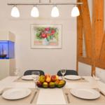 Dining room with table, chairs, and fruit bowl. Background: wall art and wooden beams.