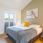 Schlafzimmer mit Bett, Wandbild und Fenster. Holzboden und Nachttisch.