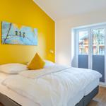 Schlafzimmer mit gelber Wand, Bett und Fenster zur Aussicht.