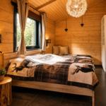 Schlafzimmer mit Holzwand, Bett mit Hirschdecke, Fenster und Schrank.