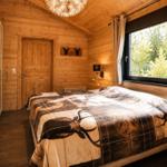 Schlafzimmer mit Holzwand, großem Fenster und Bett mit Hirschmusterdecke.