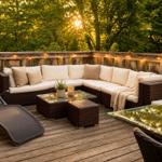 Terrasse mit Sitzgruppe, Liegestuhl und Tischen. Hintergrund: Wald bei Sonnenuntergang.