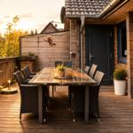 Terrasse mit Holzboden, Esstisch und Stühlen, Pflanzen und Tischlampe bei Sonnenuntergang.