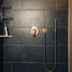 Dusche mit dunklen Steinfliesen, Duschbrause und Handbrause.