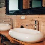 Zwei ovale Waschbecken auf massivem Holzunterschrank mit modernen Wasserhähnen.