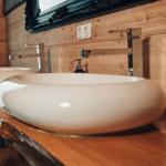 Zwei runde Waschbecken auf Holzoberfläche mit Wasserhähnen und Spiegel darüber.
