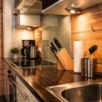 Küche mit Holzwand, Edelstahlspüle und Kochutensilien auf Arbeitsfläche.