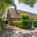 Ein zweistöckiges Haus mit Ziegeldach, umgeben von grünen Büschen und einem großen Baum.