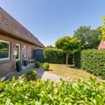 Haus mit Garten, Hecke und Baum unter blauem Himmel.