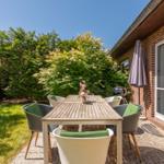 Terrasse mit Tisch, Stühlen und Grill. Hintergrund: grüne Hecke und Hauswand.