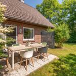 Hinterhof mit Tisch und Stühlen, Grünflächen und Blumen. Haus mit Ziegeldach und Fenstern.