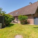 Haus mit Garten, Terrasse und Tisch mit Stühlen. Dach mit Dachfenstern und Schornstein.