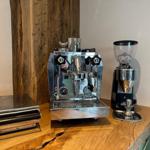 Kaffeebereitungseinrichtung auf Holztisch mit Espressomaschine, Mahlwerk und Waage.