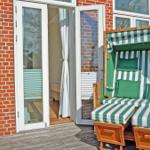 Deck with green-and-white striped lounge and wooden frame in front of red brick house.