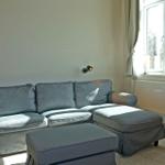 A gray sofa with cushions and footrest stands by a window.