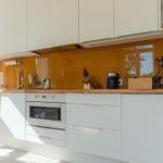 Modern kitchen with white cabinets, wooden countertop, and orange backsplash.