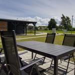 Terrasse mit Tisch und Stühlen. Hintergrund: Garten, Gebäude und Himmel.